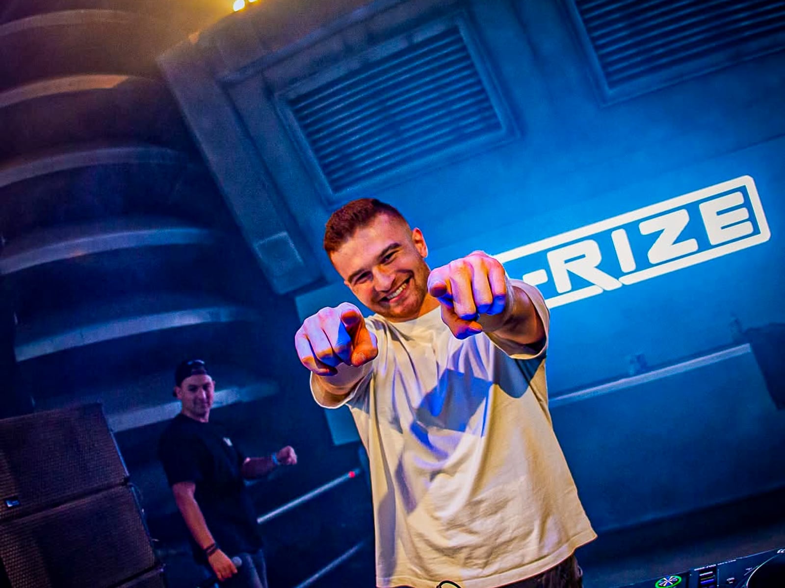 A-RIZE pointing at camera, A-RIZE logo behind